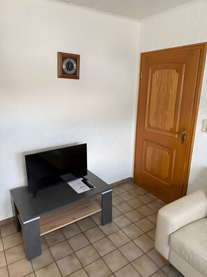 A room with a wooden door, a black TV on a table, a white couch, and a clock on the wall.