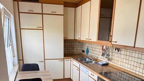 A compact kitchen with a dining table, a black chair, a built-in oven, and a window with curtains.