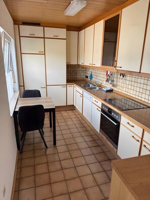 Cocina compacta con una mesa de comedor, una silla negra, horno empotrado y una ventana con cortinas.