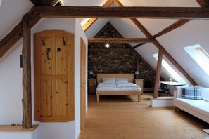 Un dormitorio con techo inclinado, vigas de madera, pared de piedra, cama, mesitas de noche y un sofá.