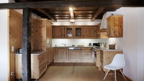 Een keuken met houten kastjes, een witte stoel en een plafondlamp.