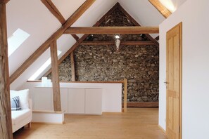 A loft-style room with a sloped ceiling, exposed wooden beams, a stone wall, and a white bench.