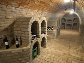 Une cave à vin avec des arches en pierre, des bouteilles de vin et un sol en briques.