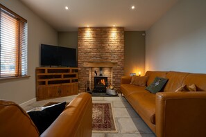 A living room with a stone fireplace, a television, a leather sofa, and a wooden entertainment unit. - The Old Pitman's House - near Sherwood Forest, Spacious modern home (New Ollerton)