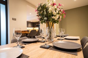 Una mesa de comedor dispuesta con platos, cubiertos y copas de vino, con un florero en el centro.