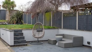Un patio con un sofá de mimbre, una silla colgante y una mesita.