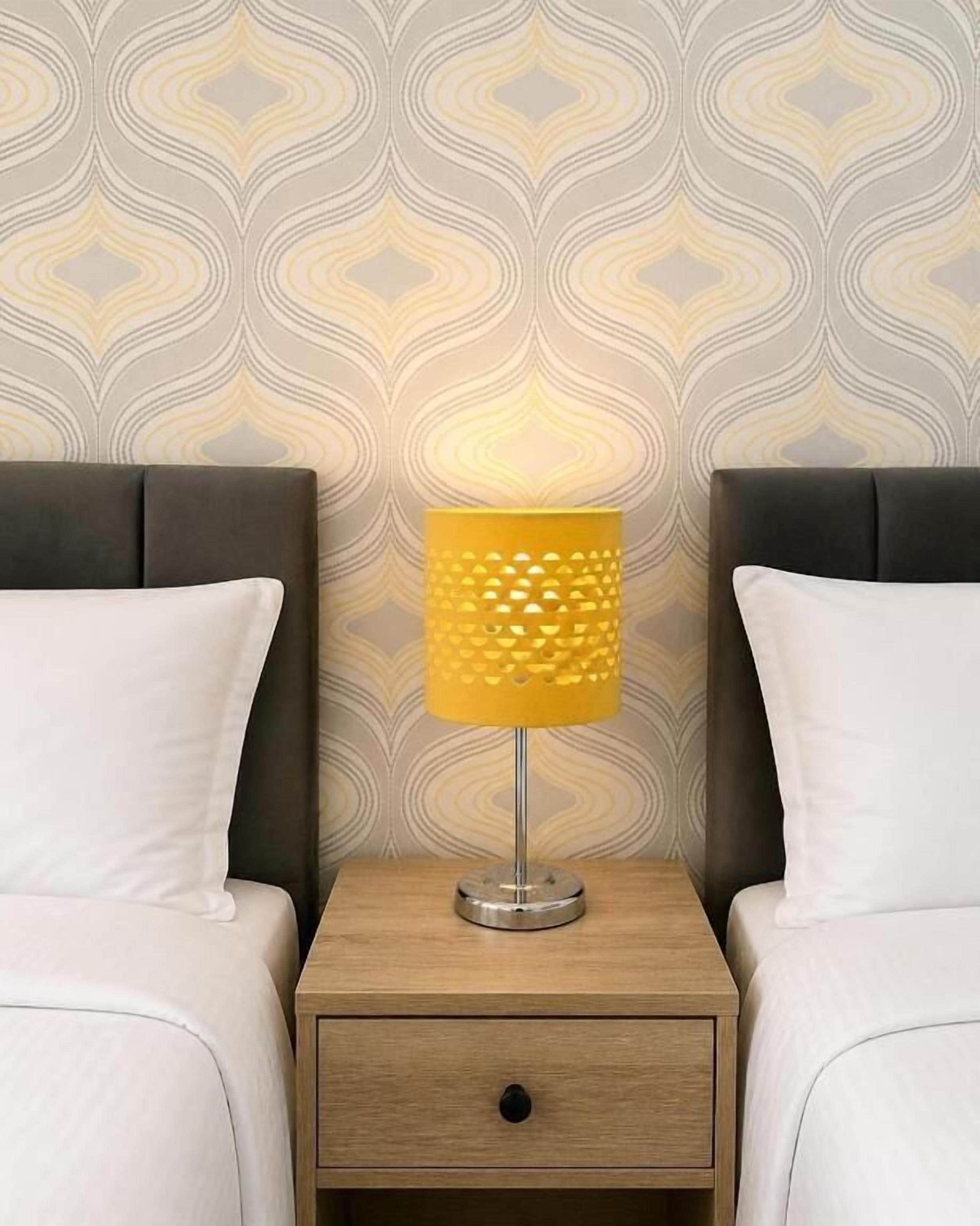 A bed with a headboard, a bedside table with a lamp, and a patterned wallpaper.