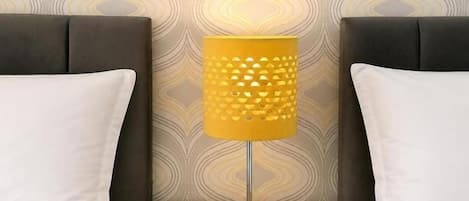 A bed with a headboard, a bedside table with a lamp, and a patterned wallpaper.