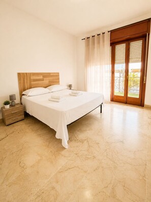 A bedroom with a bed, a nightstand, a lamp, a potted plant, and a sliding glass door leading to an outdoor area. - Vrbo Property (Milazzo)