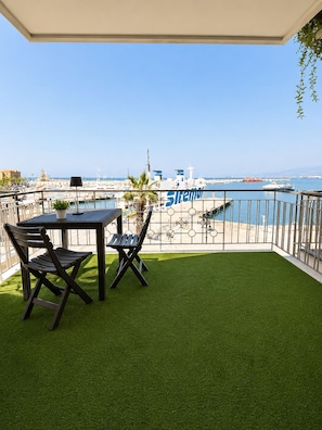 A balcony with artificial grass, a table, two chairs, and a view of a marina with boats and a lighthouse. - Vrbo Property (Milazzo)