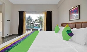 A hotel room with a bed, a view of palm trees, and a balcony. - GRAND VISTARA AIRPORT SUITES (Nedumbassery)