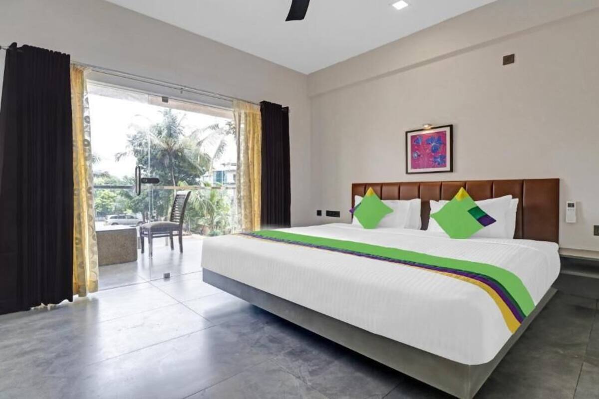 A hotel room with a large bed, a view through a glass door, and a painting on the wall.