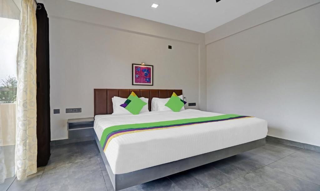 A hotel room with a large bed, a headboard, a framed picture on the wall, and a window with curtains.