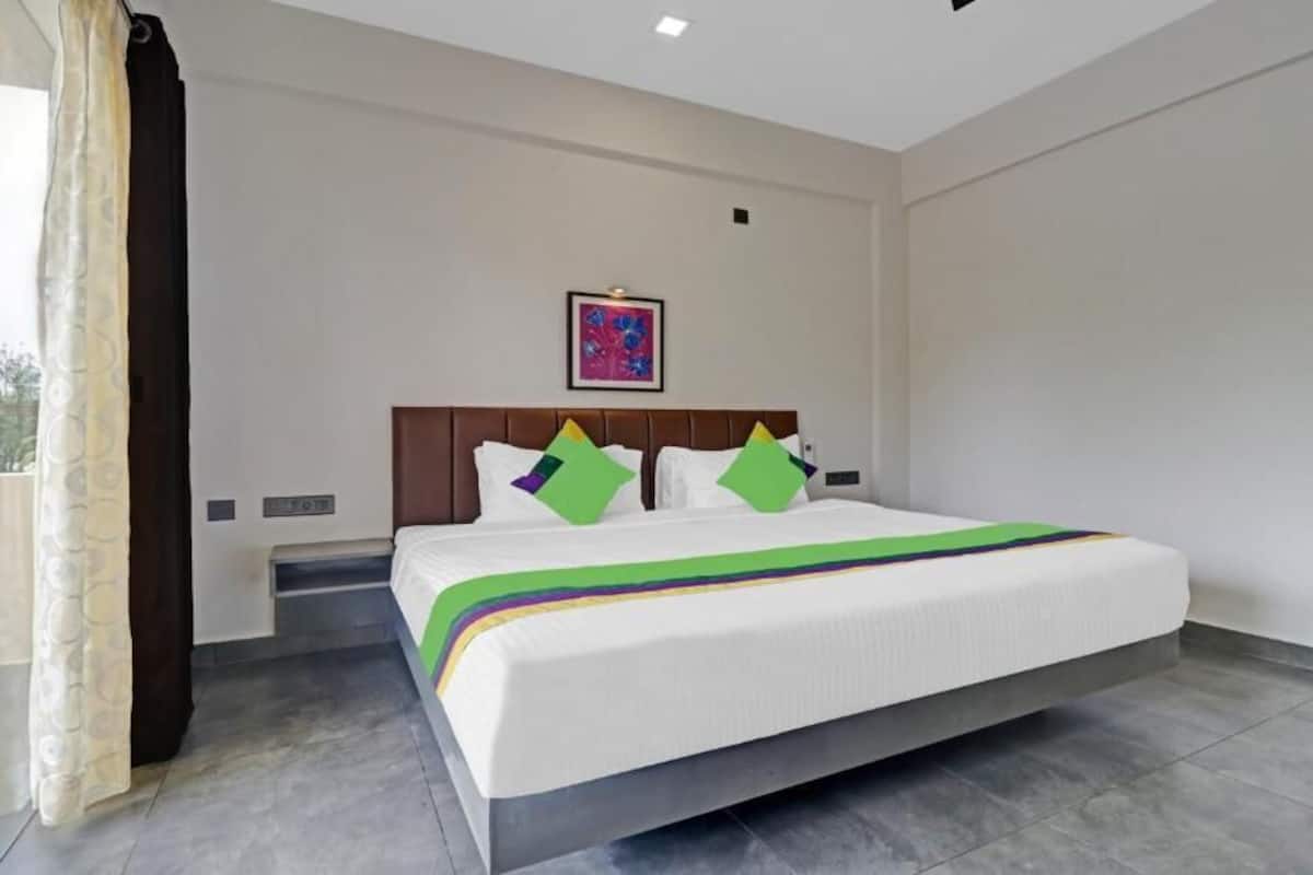 A hotel room with a large bed, a headboard, a framed picture on the wall, and a window with curtains.