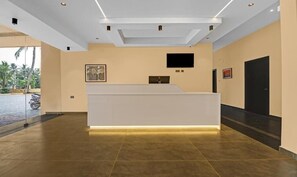 A reception area with a reception desk, a flat-screen TV, and a door. - GRAND VISTARA AIRPORT SUITES (Nedumbassery)