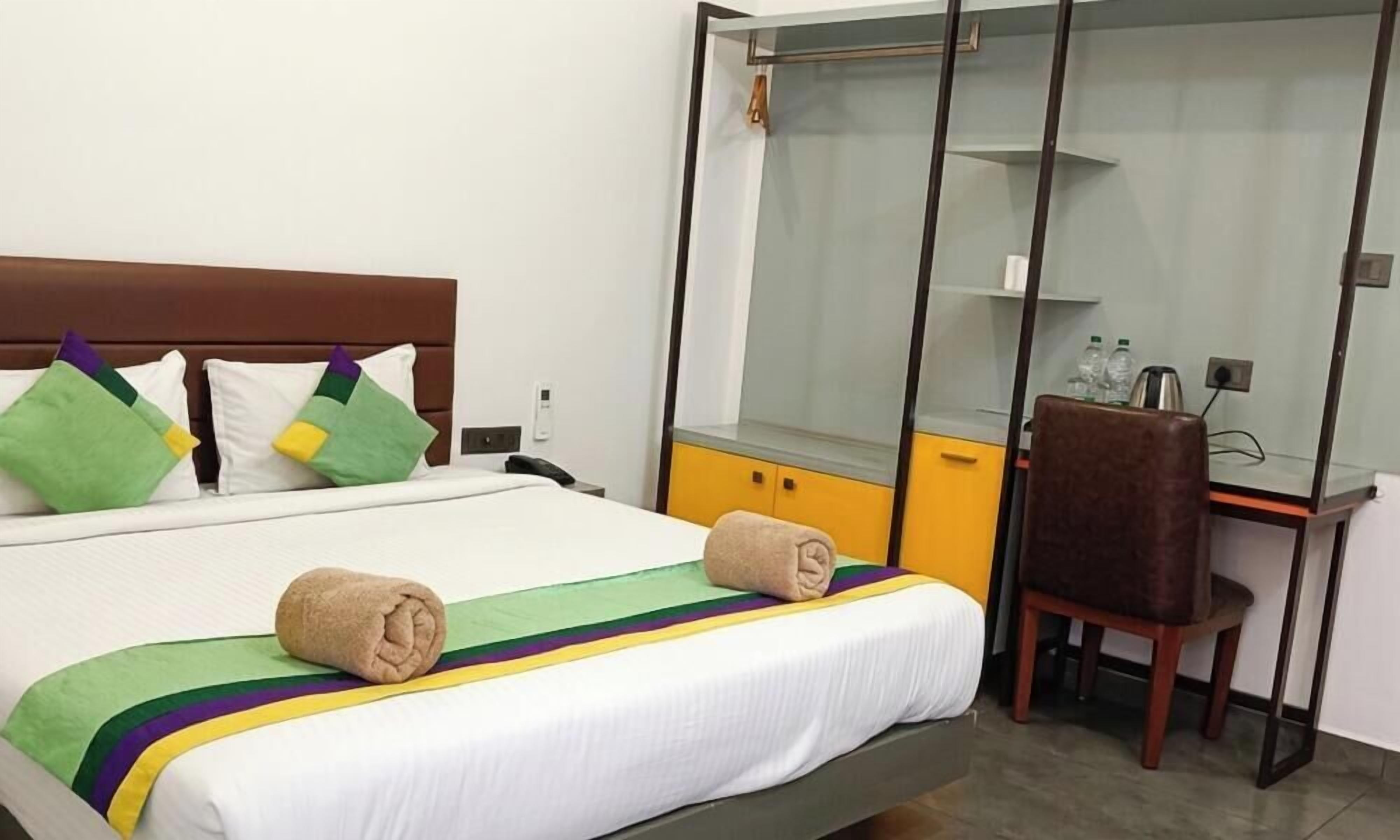A hotel room with a bed, a desk, a chair, a wardrobe, and a mirror.