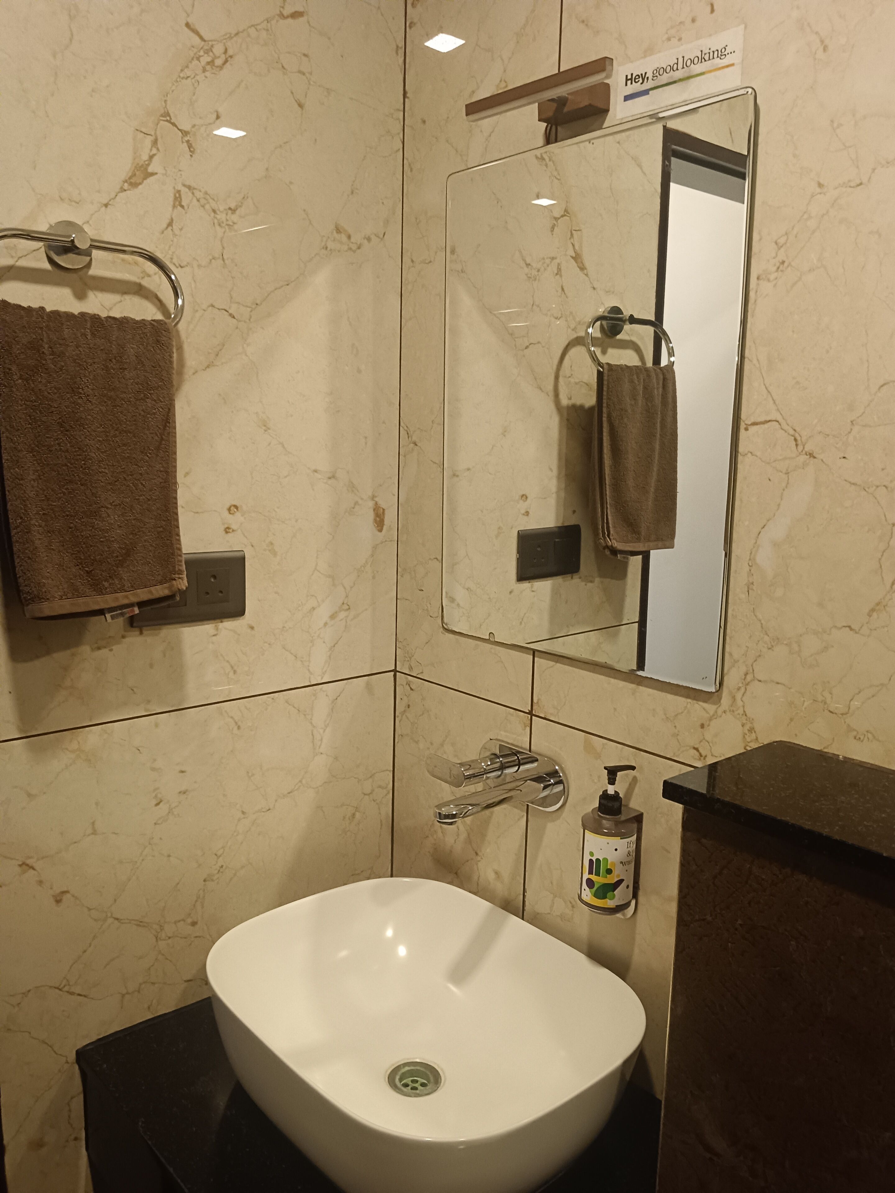 Ein Badezimmer mit einem weißen Waschbecken, einem Spiegel, einem Handtuchhalter und einer Seifenspender.