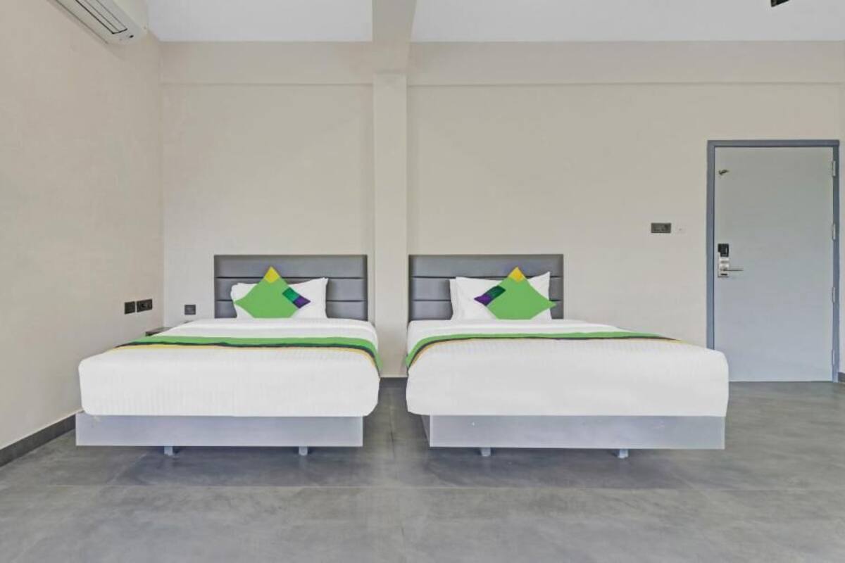 A hotel room with two beds, a door, and a light switch on the wall.