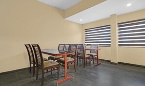 A dining area with a table and chairs, a ceiling with recessed lighting, and windows with horizontal blinds. - GRAND VISTARA AIRPORT SUITES (Nedumbassery)