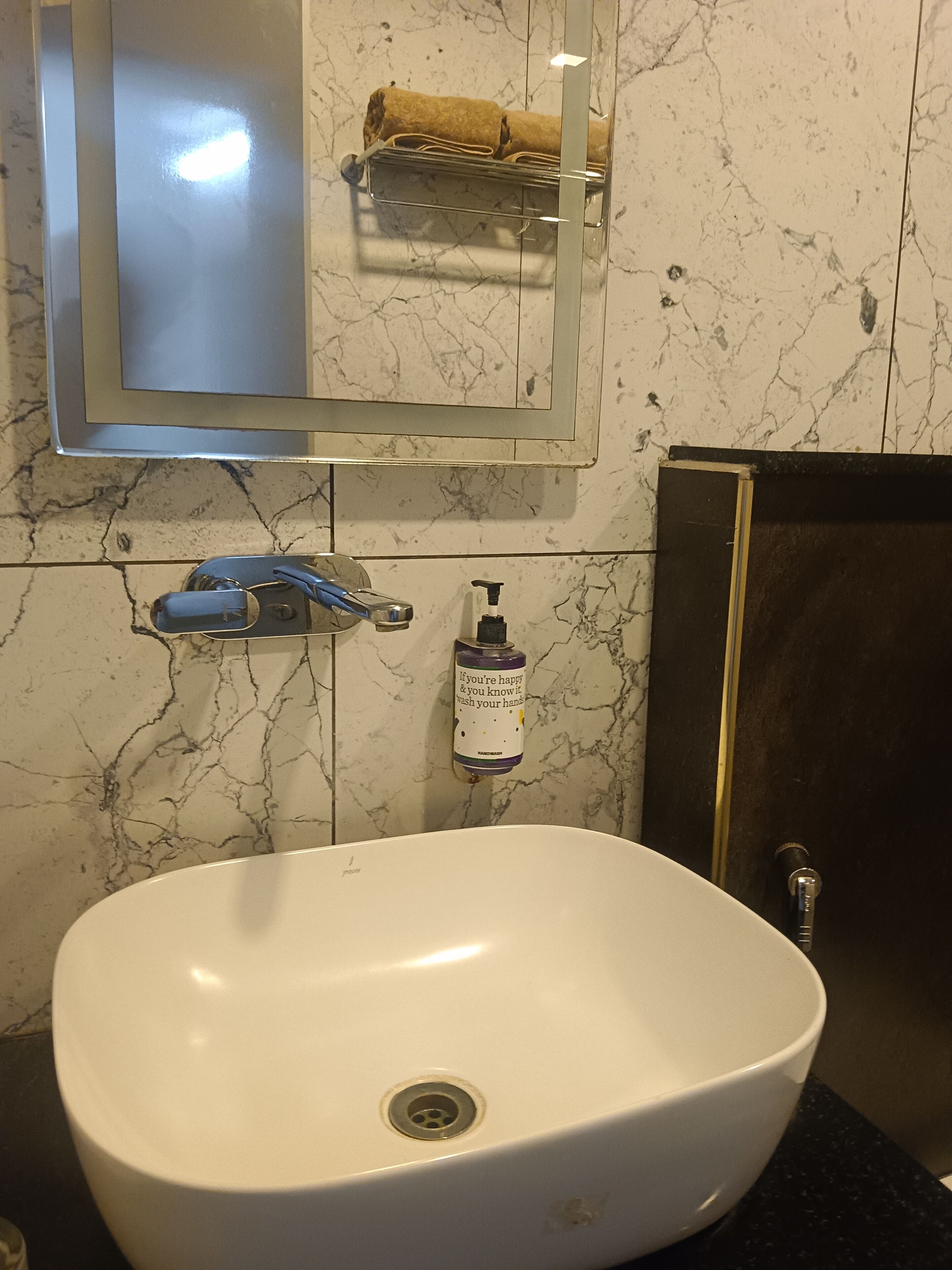 Ein Badezimmer mit einem weißen Waschbecken, einem Spiegel, einem Handtuchhalter, einer Seifenspender und einem dunklen Schrank.
