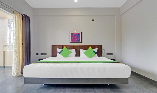 Una habitación de hotel moderna con una cama grande, cabecera con almohadones decorativos, un cuadro en la pared y vistas al exterior por una ventana.