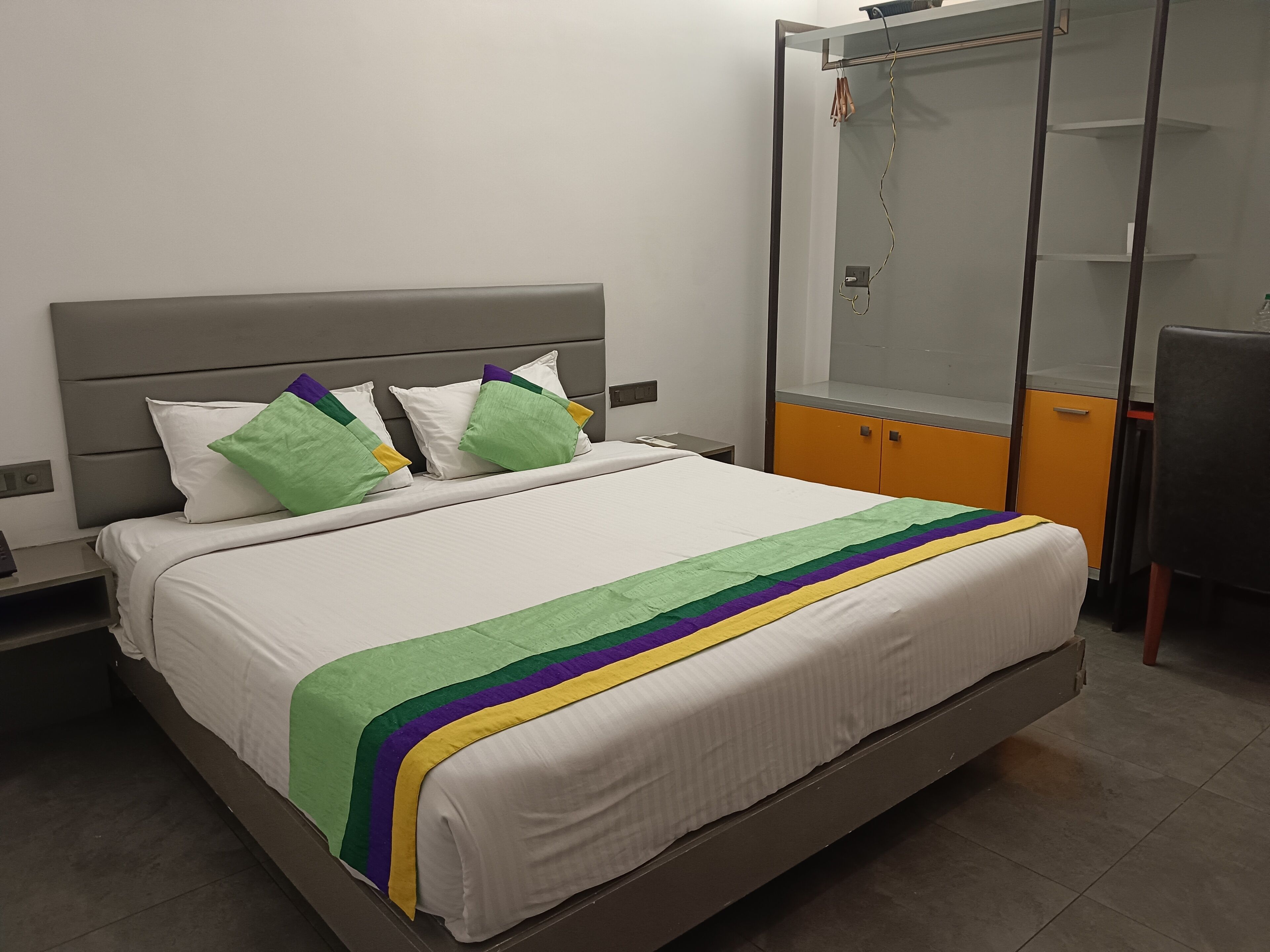 Un lit avec un matelas blanc, une tête de lit grise et des coussins colorés.