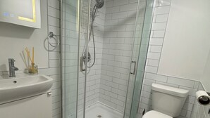 Et moderne badeværelse med en glasafskærmet brusekabine, en hvid vask og et toilet.