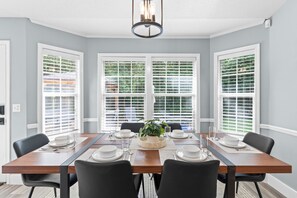 A dining room with a wooden table set for four, white chairs, and a central plant. - Spillway Oasis- Plunge Pool & Fire Pit (Dothan)