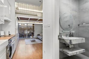 A modern kitchen with a washing machine, a dining area with a table and chairs, and a bathroom with a large mirror and marble sink. - Scandinavian Loft Escape in JVC Dubai (Dubai)