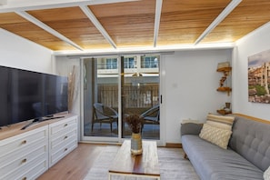 A living room with a flat-screen TV, a sofa, a coffee table, and a sliding glass door leading to a balcony with chairs. - Scandinavian Loft Escape in JVC Dubai (Dubai)