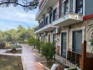 A residential building with multiple balconies, a paved pathway, and small trees. - Lotus 4 Mevsim Otel (Ayvalık)
