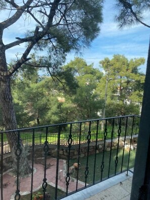 A balcony with a view of a park, a stone pathway, and a body of water. - Lotus 4 Mevsim Otel (Ayvalık)