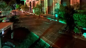 Un immeuble à plusieurs étages doté de balcons, de climatiseurs et d’un espace d’entrée pavé agrémenté de verdure.