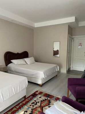 Habitación de hotel con dos camas, un sillón morado, un tapete estampado y una puerta con un letrero de 'No Fumar'.