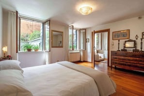 Ein Schlafzimmer mit Bett, Kommode, Spiegel und Fenster mit Blick ins Grüne.