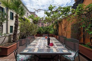 Un espacio exterior para comer con una mesa a cuadros, sillas y una botella de vino.
