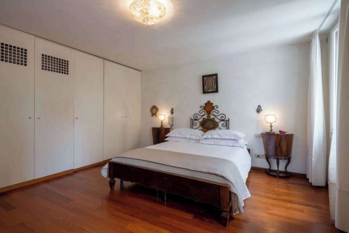 Une chambre à coucher avec un lit en bois, des murs blancs, un luminaire au plafond et deux tables de chevet avec des lampes.