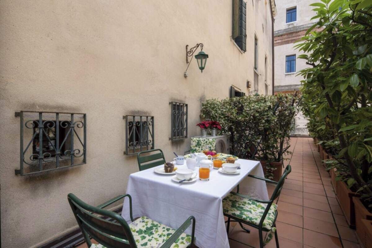 Une table dressée pour le petit-déjeuner, avec des chaises, une nappe blanche et une plante en pot.