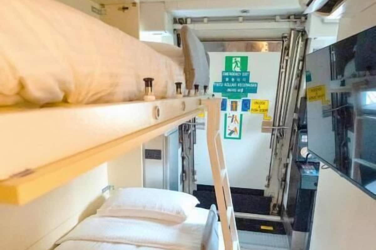 Un compartiment de train étroit, équipé de lits superposés, d’une échelle et d’un petit coin cuisine.
