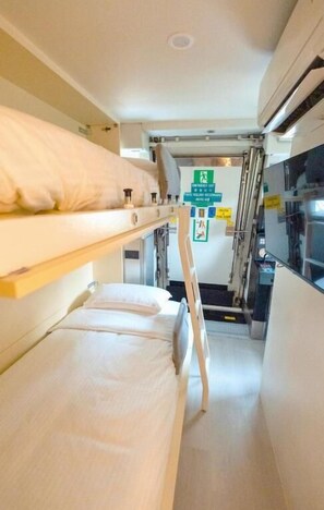 A narrow train compartment with bunk beds, a ladder, and a small kitchenette. - Train Pod at one-north (Singapore)
