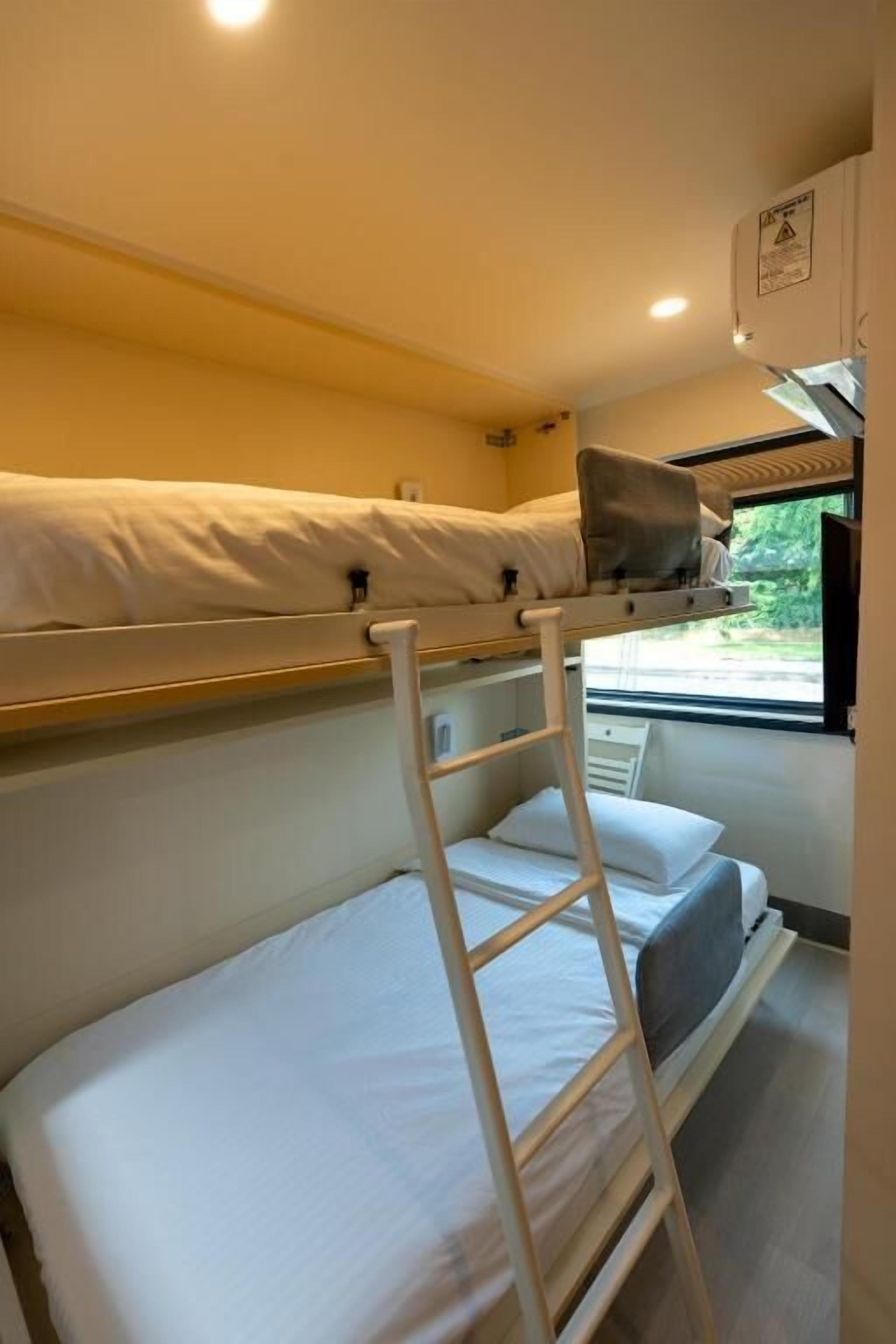 A bunk bed room with a ladder, a window, and a small kitchenette.