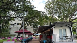 An outdoor seating area with tables and chairs, a covered seating section, and a building in the background. - Train Pod at one-north (Singapore)