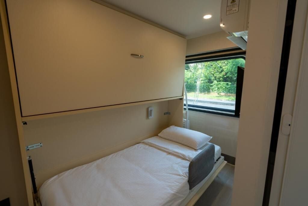 A small, single-bed room with a window providing a view of greenery outside.