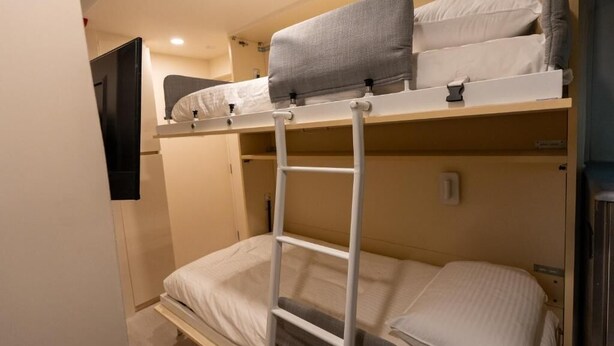 A bunk bed with a ladder, a flat bed below, and a wall-mounted TV. - Train Pod at one-north (Singapore)