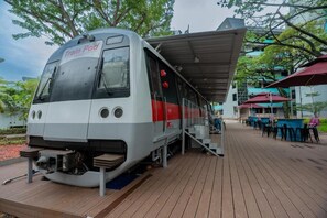 Un tren cápsula detenido con una plataforma cubierta, asientos al aire libre y un edificio al fondo.