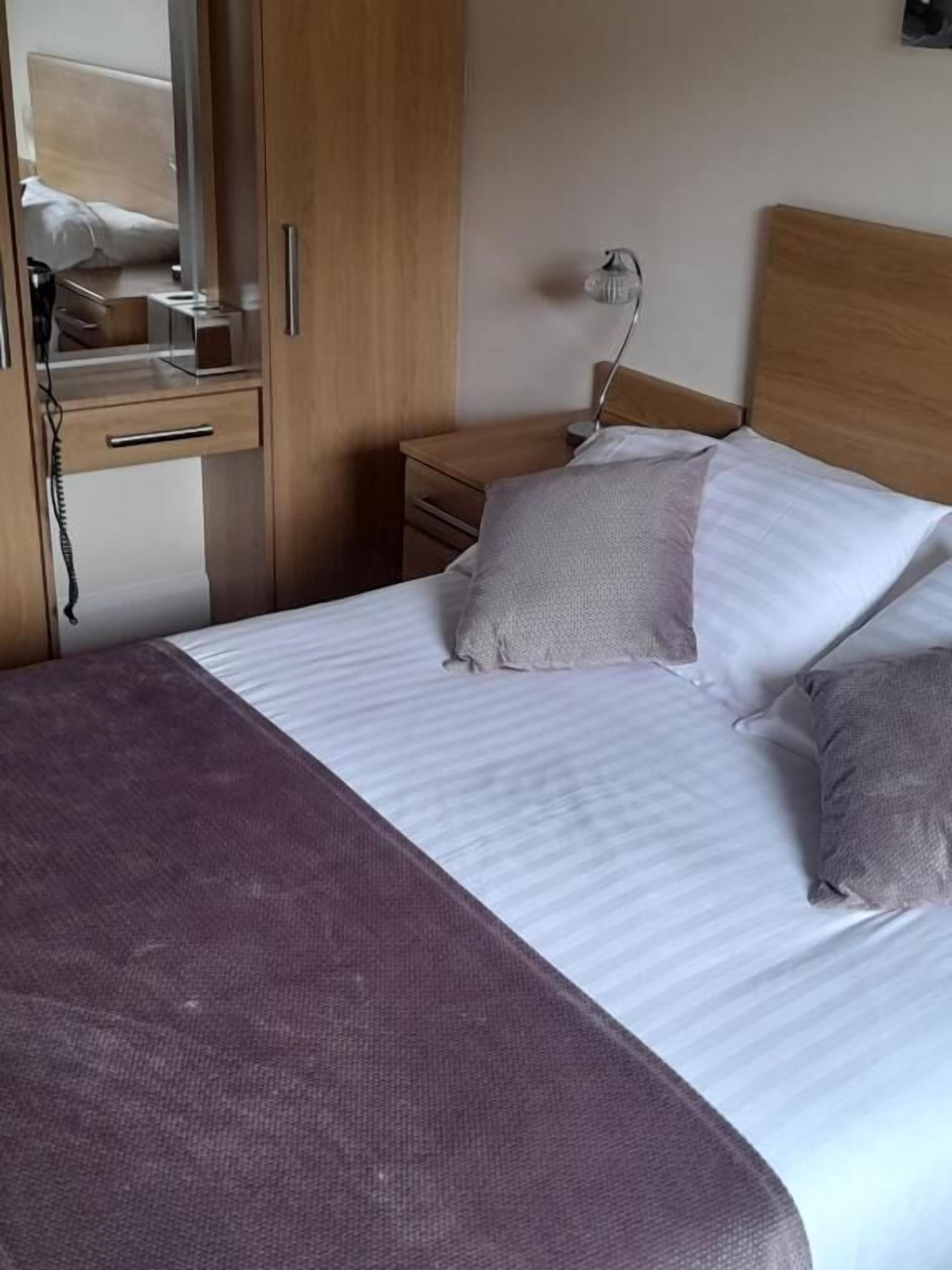 A bedroom with a bed, a nightstand, a lamp, a wardrobe, and a mirror.