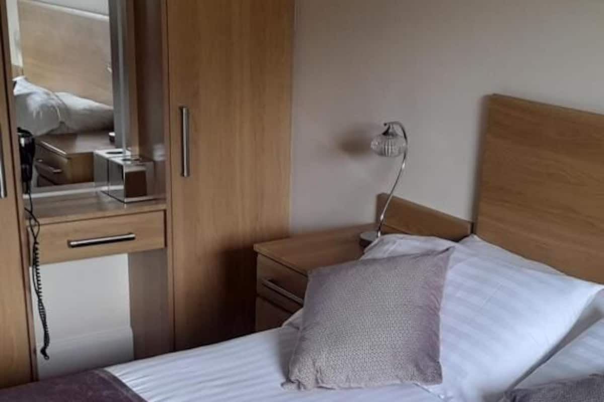 A bedroom with a bed, a nightstand, a lamp, a wardrobe, and a mirror.