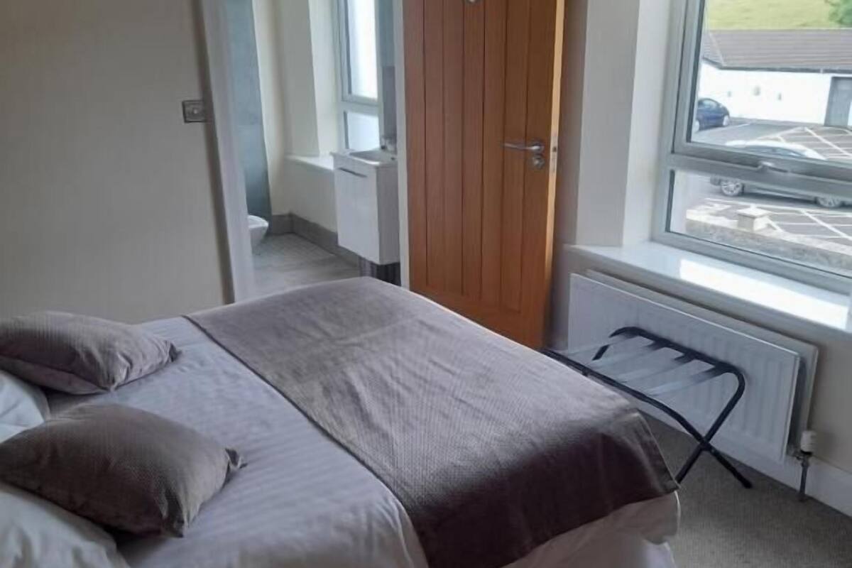 A bedroom with a bed, a radiator, a window with a view, and a door leading to another room.