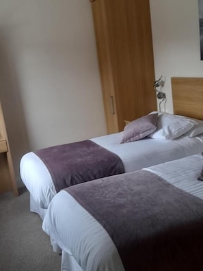 A bedroom with two beds, a wooden wardrobe, and a small decorative item on the wall.