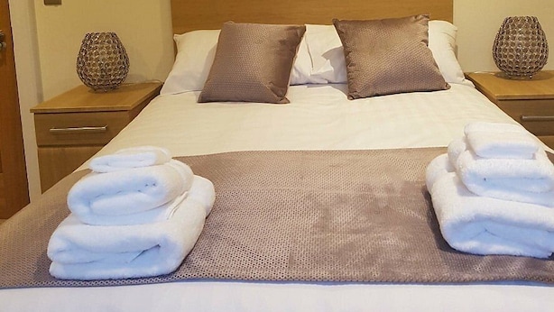Una cama bien hecha con almohadas, una manta y toallas dobladas sobre un edredón texturizado.